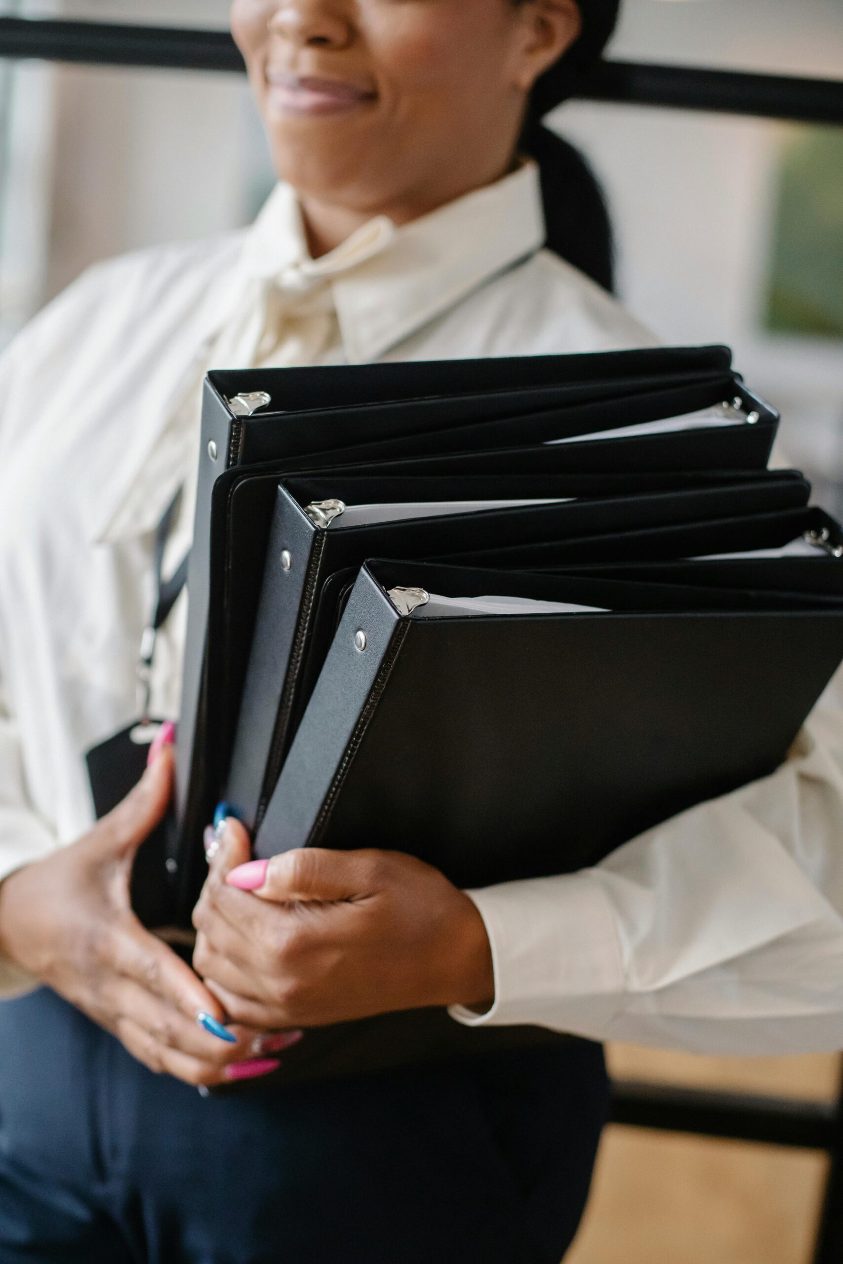 pexels-photo-5668873-5668873 Professional woman in formal attire carrying multiple black folders indoors.